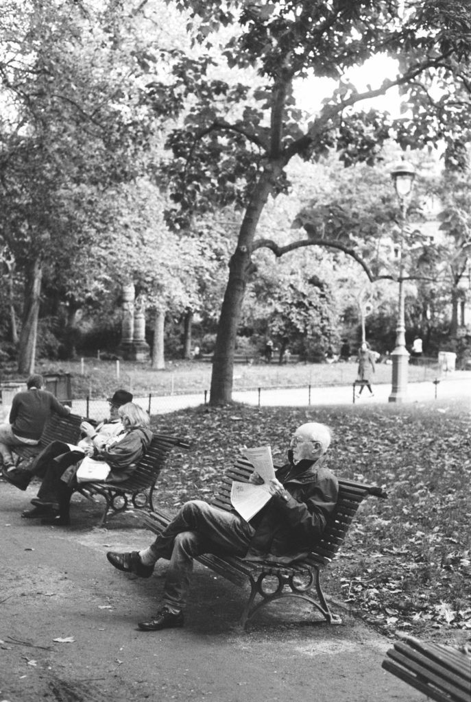 An old gentleman reads the newspaper in the park in Paris, France. Shot on Kodak Tri-x 400 film by Holly Michon Photography. 