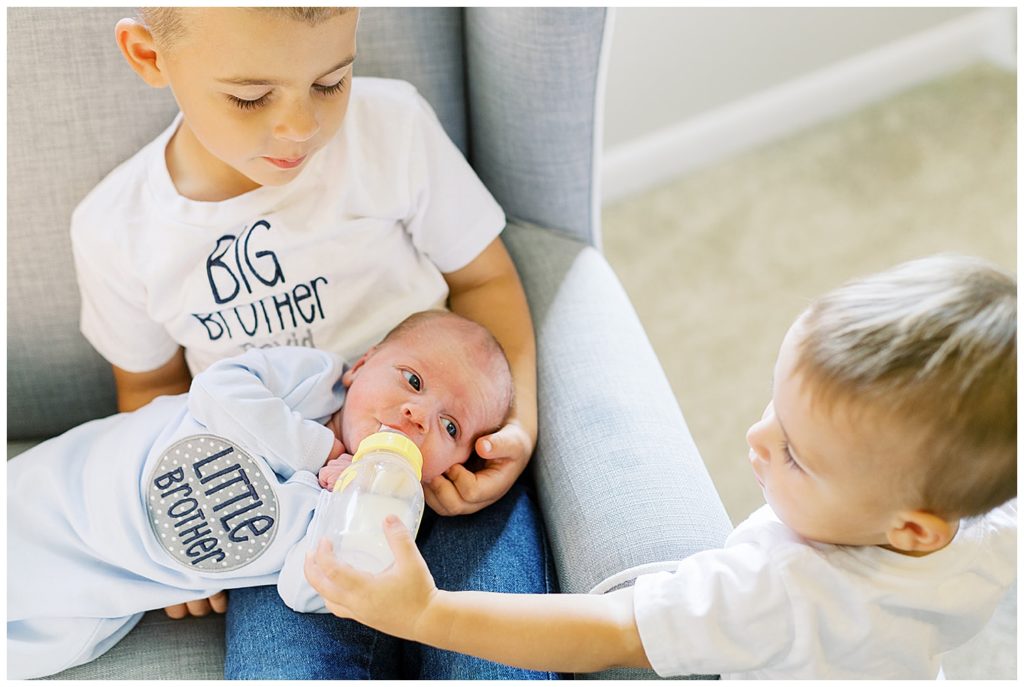 Proud big brothers help feed their newborn baby brother in this Knoxville family portrait session at home. Photo by Holly Michon Photography