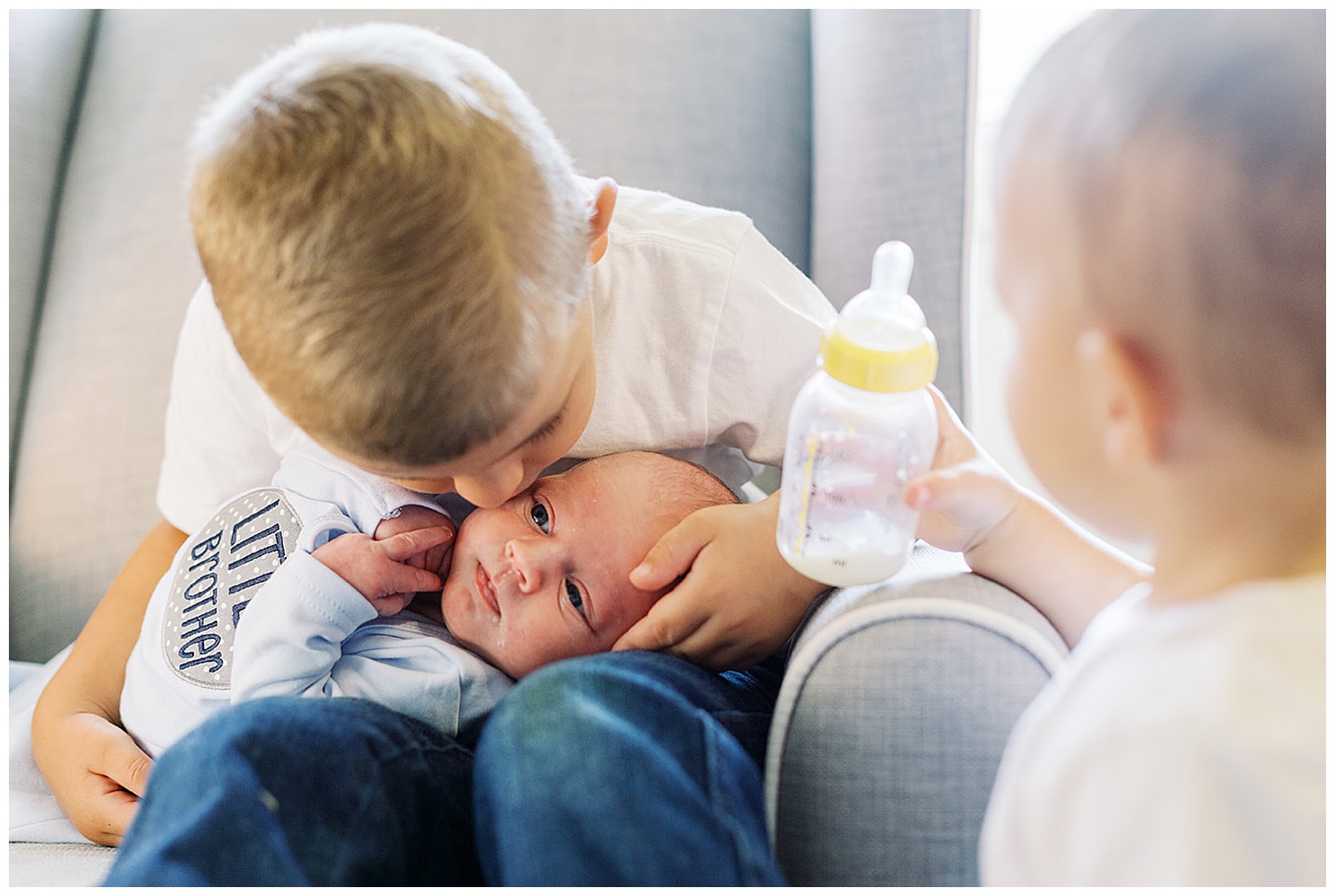 Knoxville in home newborn family session. Older brother kisses newborn baby brother and feeds him a bottle.
