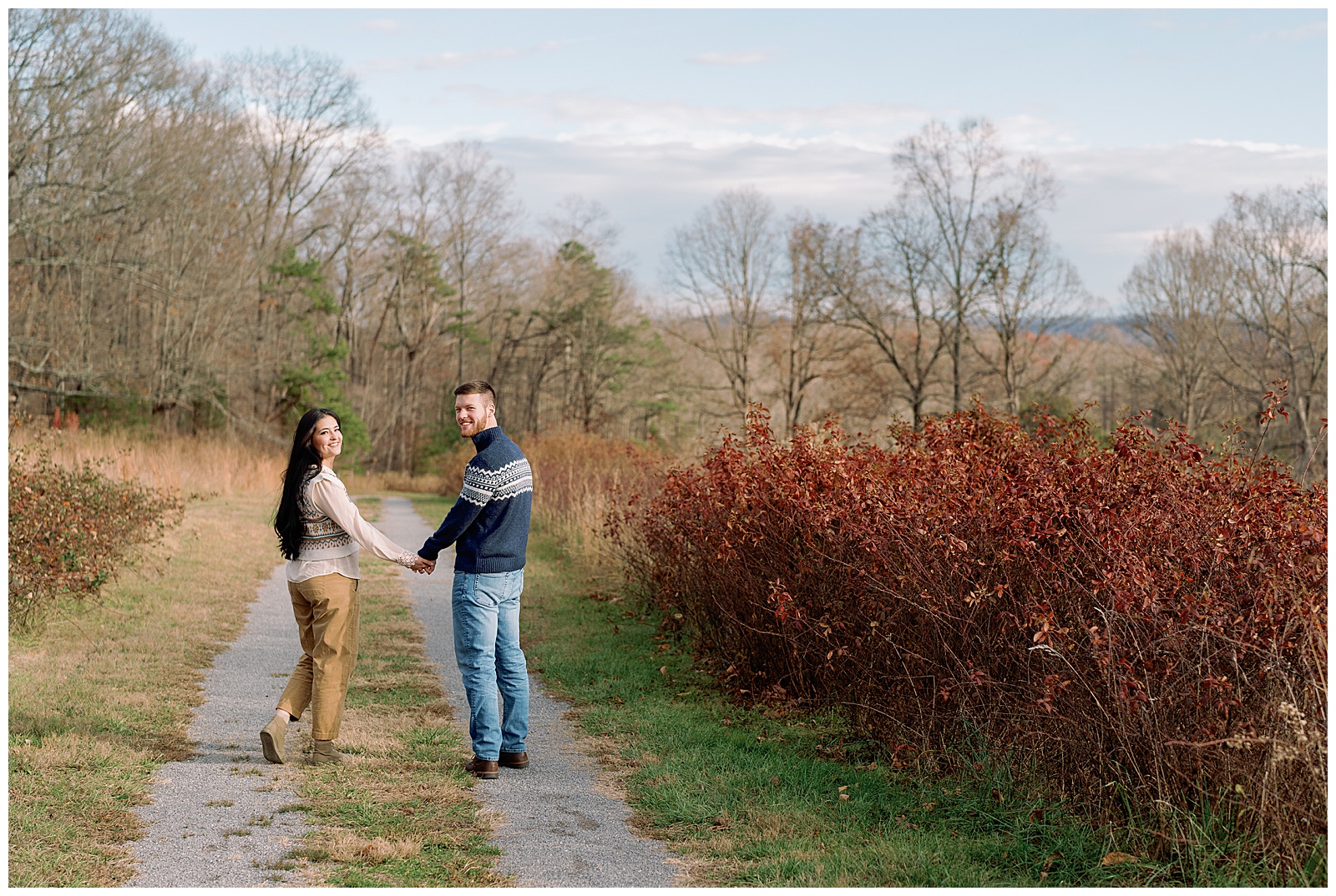 Engaged man and woman wearing sweaters in winter walking holding hands at their farm engagement session.