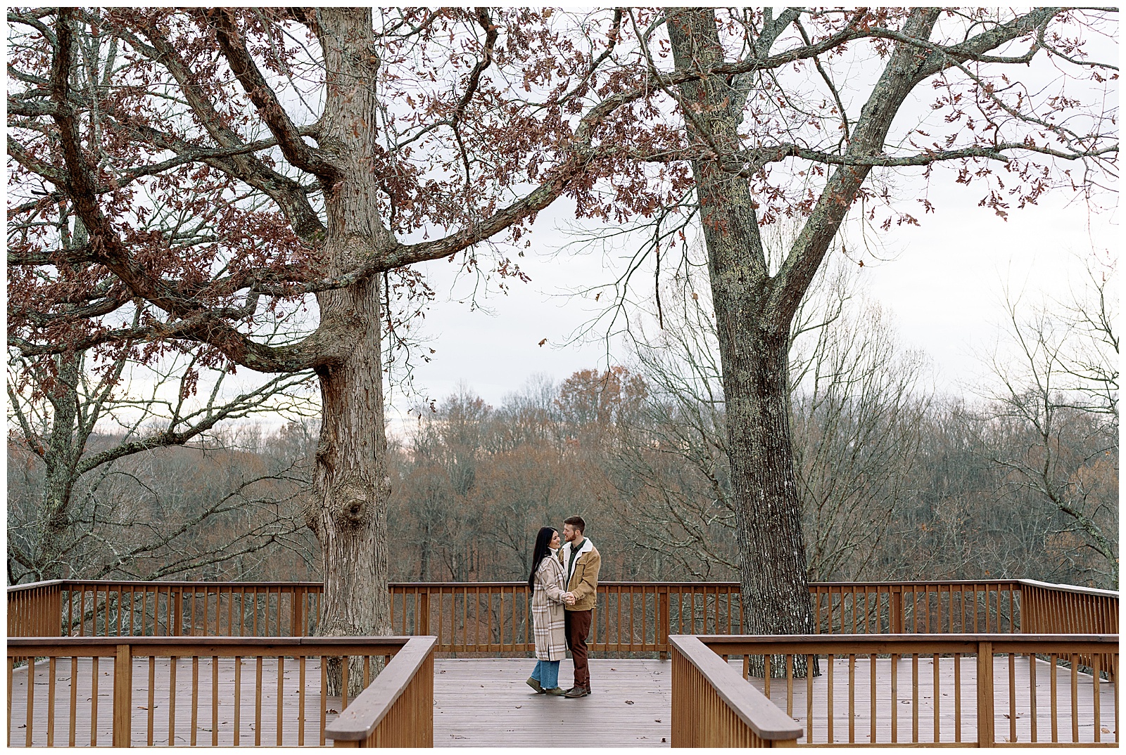 Engaged man and woman wearing winter coats in winter dancing under trees at their farm engagement session.