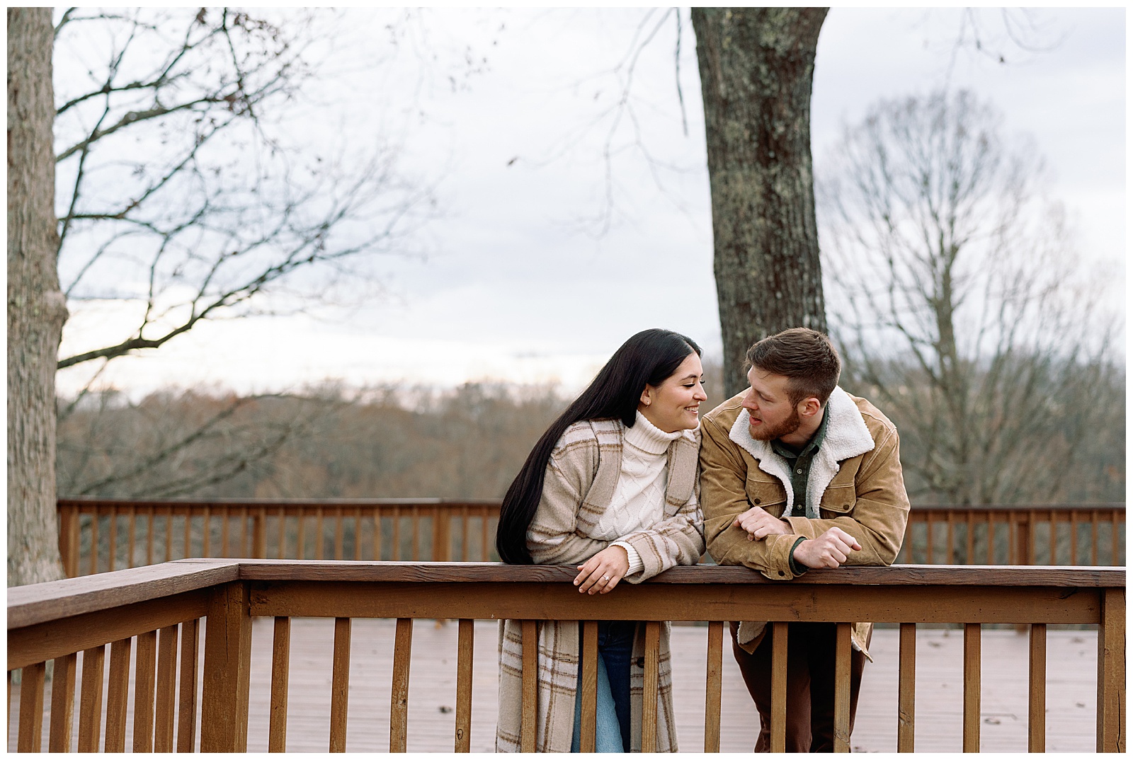 Engaged man and woman wearing winter coats in winter snuggled up to each other at their farm engagement session.