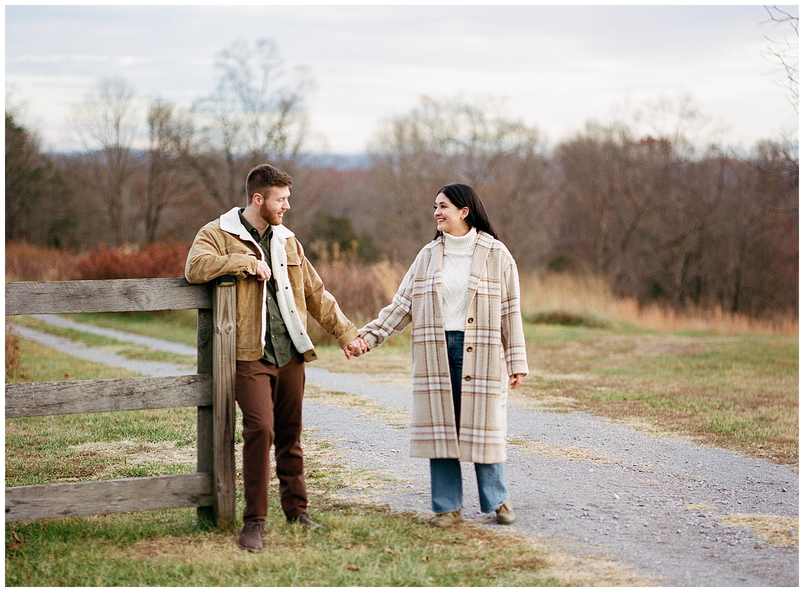 Engaged man and woman wearing winter coats in winter holding hands at their farm engagement session.