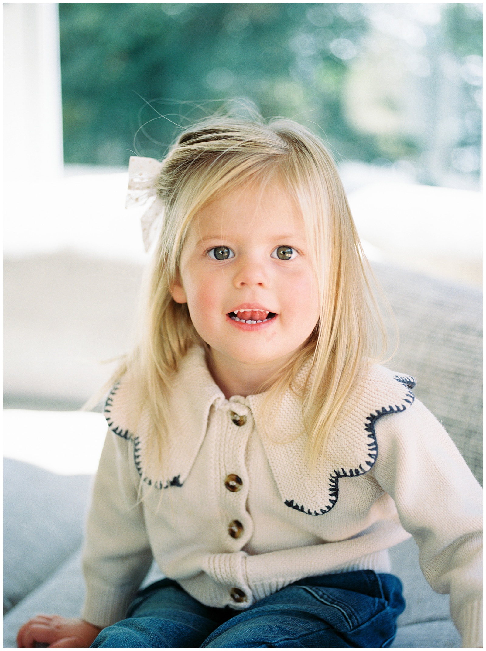 Adorable little girl smiles at the camera in a light filled sunroom 
