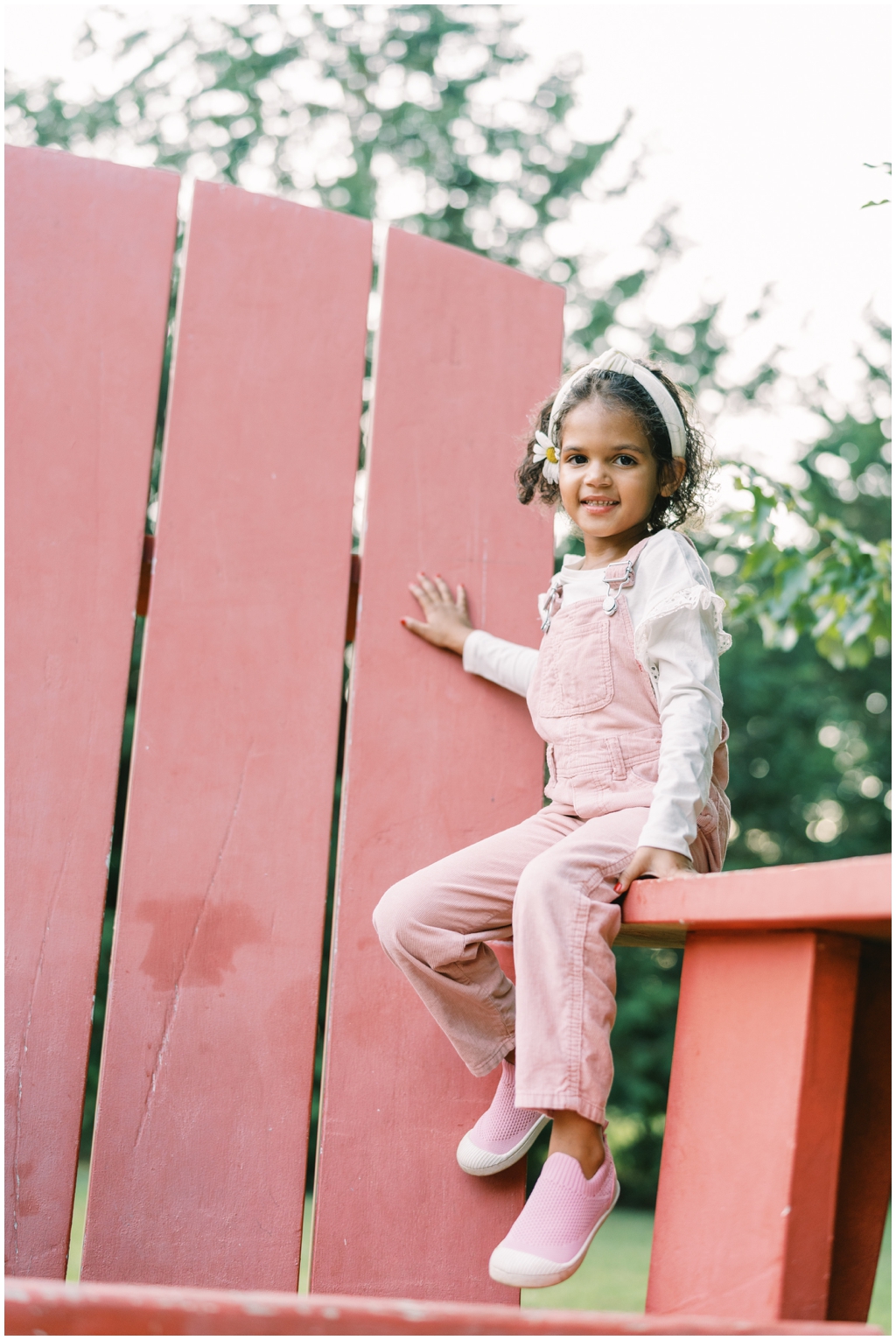 Adorable little girl sitting on large red lawn chair at the Knoxville Botanical Gardens for family photo session