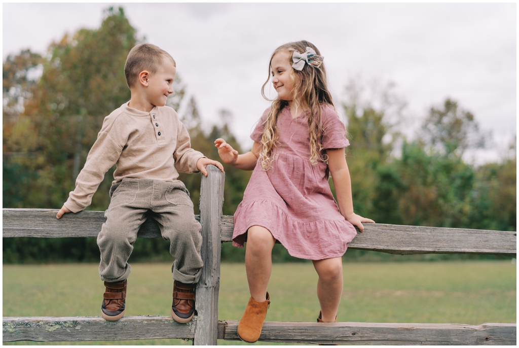 Adorable brother sister duo sitting on fence together during fall family session in Knoxville, TN.