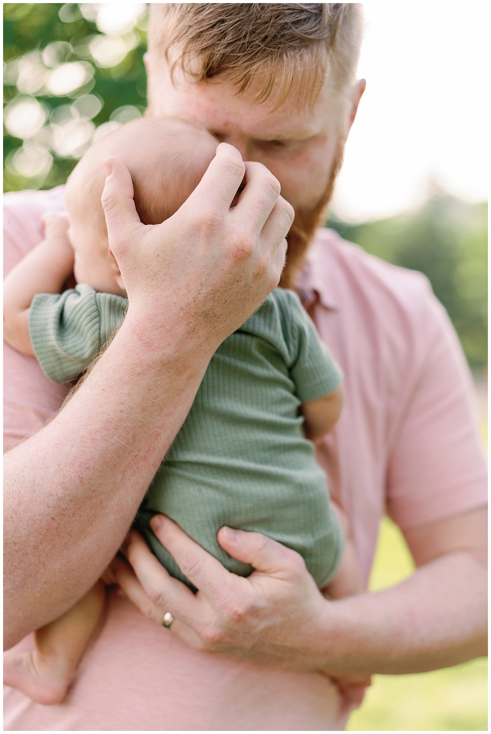 Dad holds newborn son in embrace during outdoors family session in Knoxville, TN.