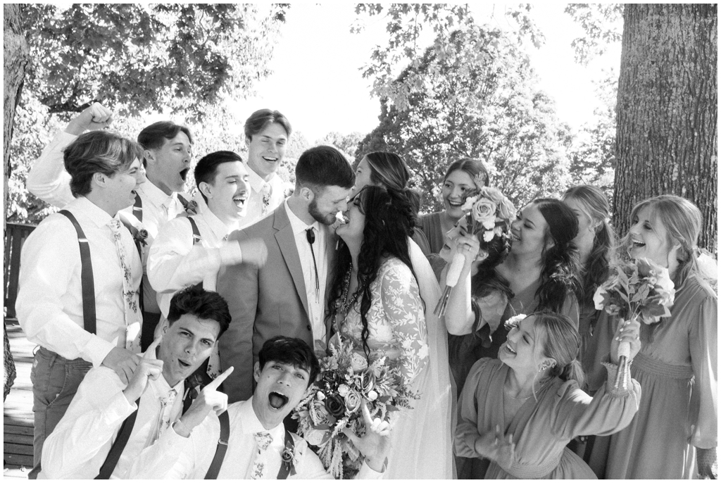 Black and white image of wedding party celebrating while the bride and groom laugh with each other.