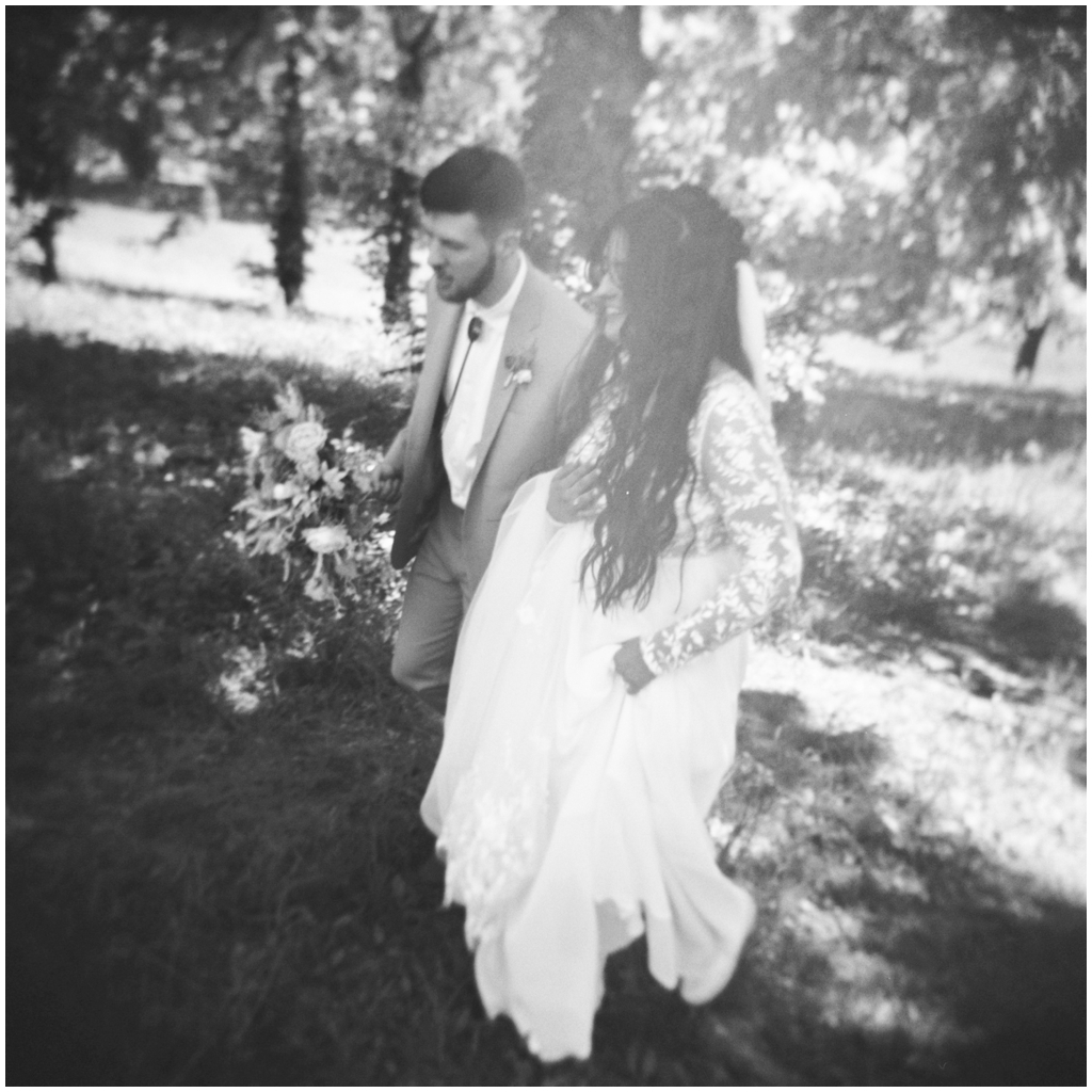 Black and white film image of bride and groom walking in nature.