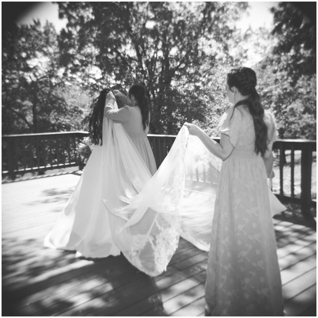 Bridesmaids adjust brides veil in black and white film image.