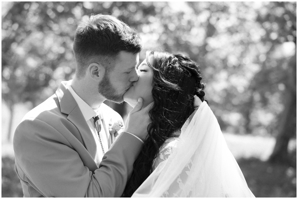 Black and white image of bride and groom kissing in sunny meadow.