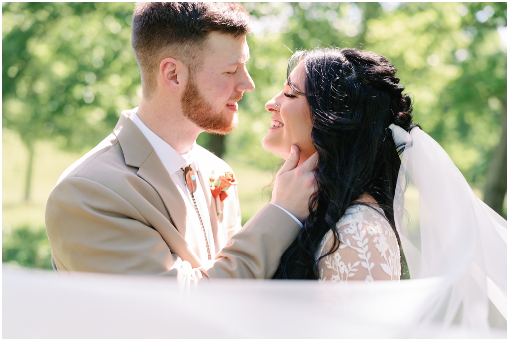 Colorful image of bride and groom sharing a loving moment in sunny field.