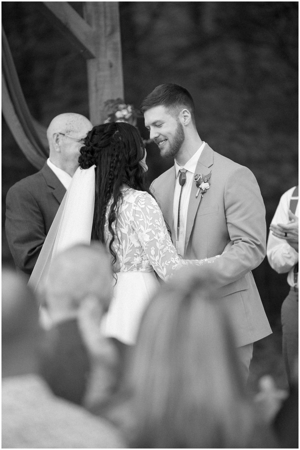 Bride and groom smile at each other in black and white image during ceremony.