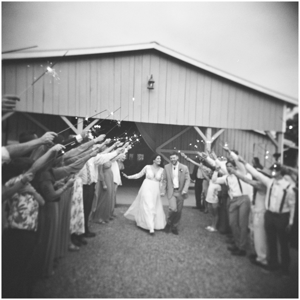 Black and white image of bride and groom kissing while exiting the wedding with sparklers. 