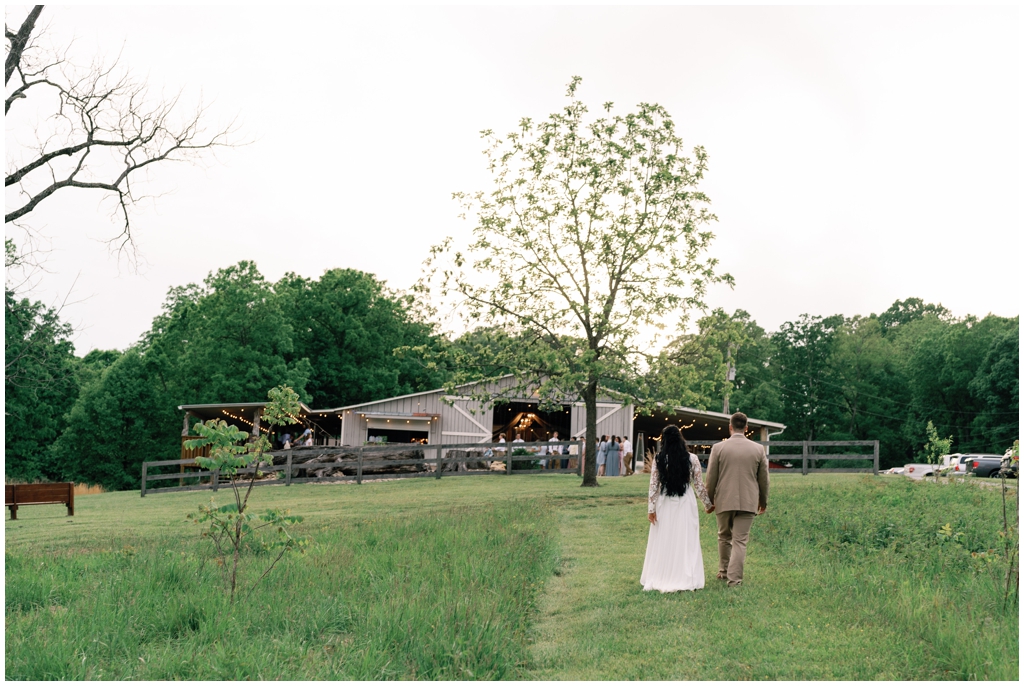 Bride and groom look at reception barn from afar during colorful and sentimental Knoxville spring wedding.