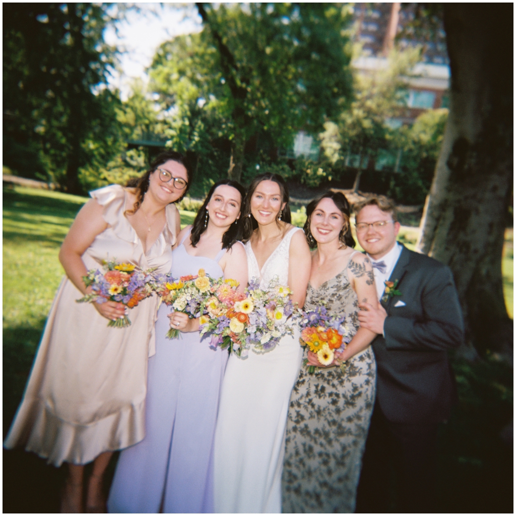 Film image of bridal party leaning on each other after reception at classy summer Maryville, TN wedding.