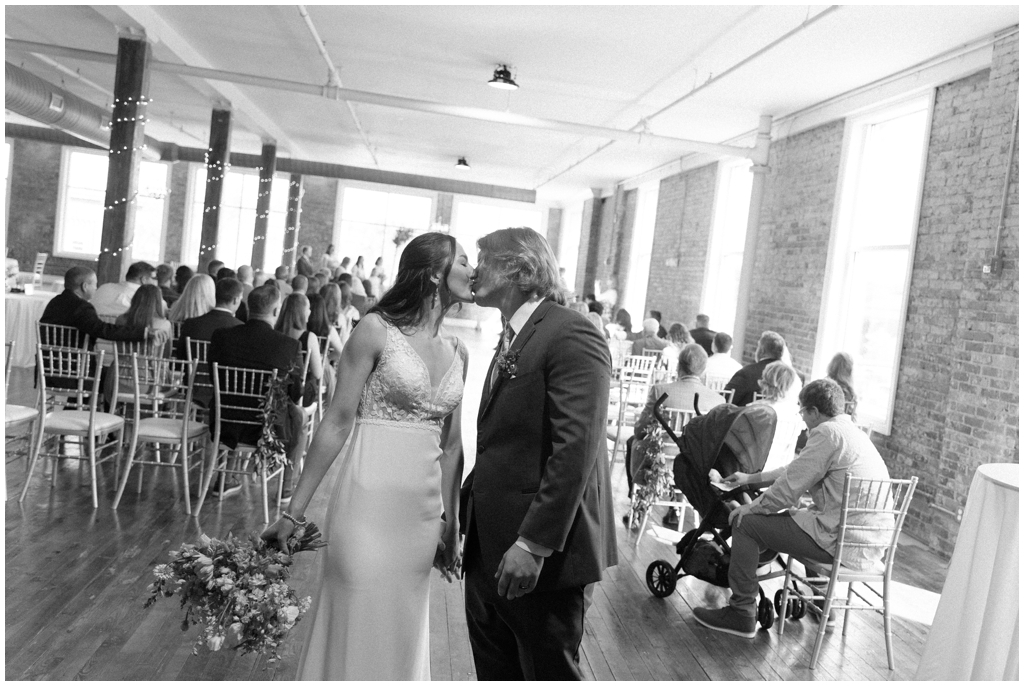 Black and white image of bride and groom kissing at end of aisle during classy and romantic Maryville, TN wedding.