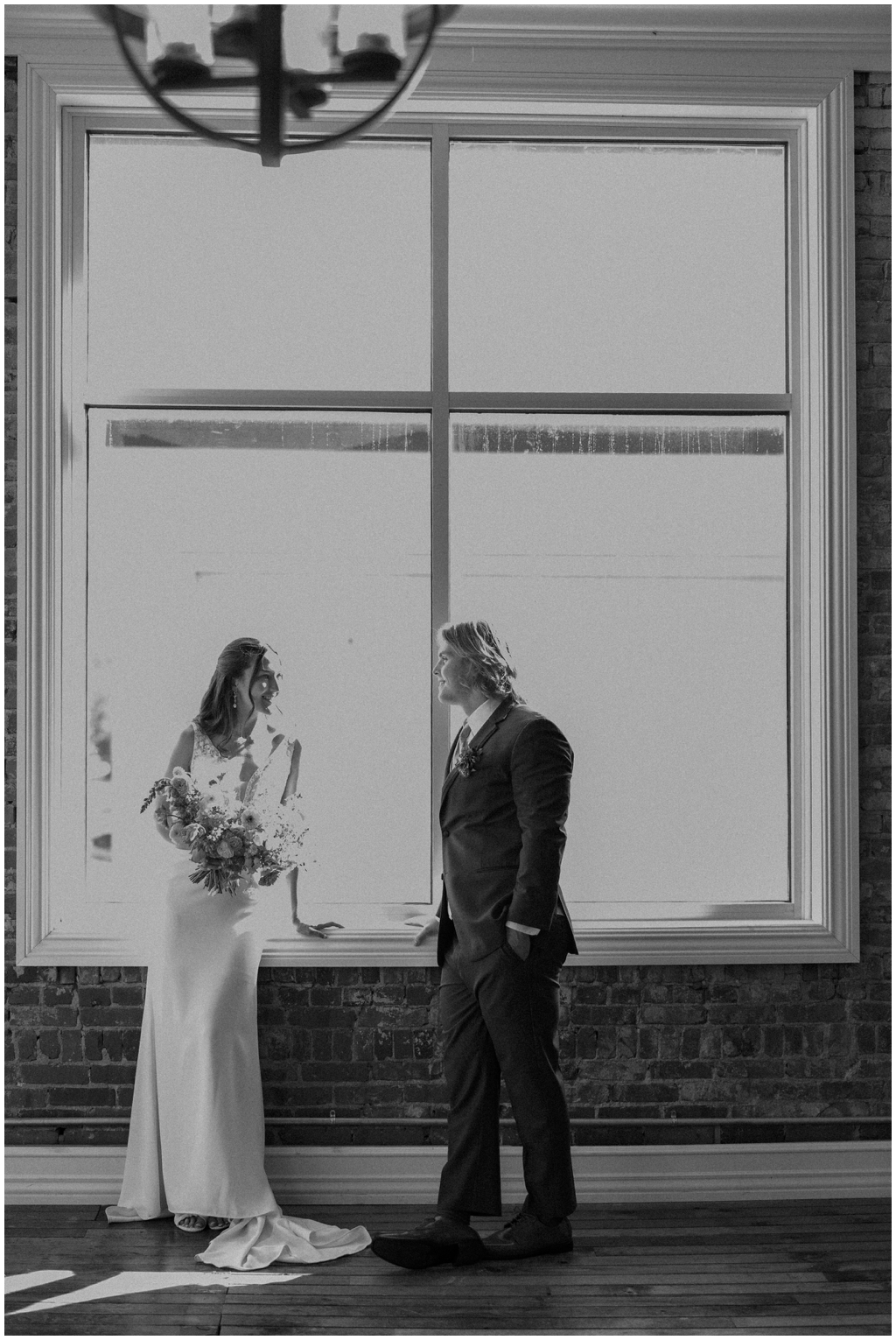 Black and white image of bride and groom smiling in front of window during classy and romantic summer Maryville wedding.