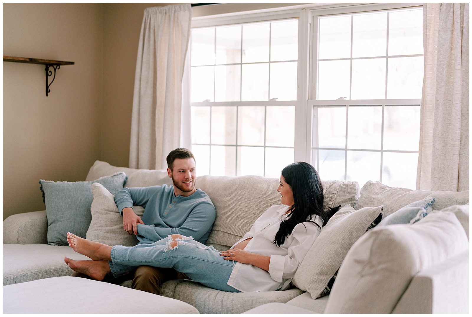 Mom and dad sit on couch in first home during timeless Knoxville maternity session.