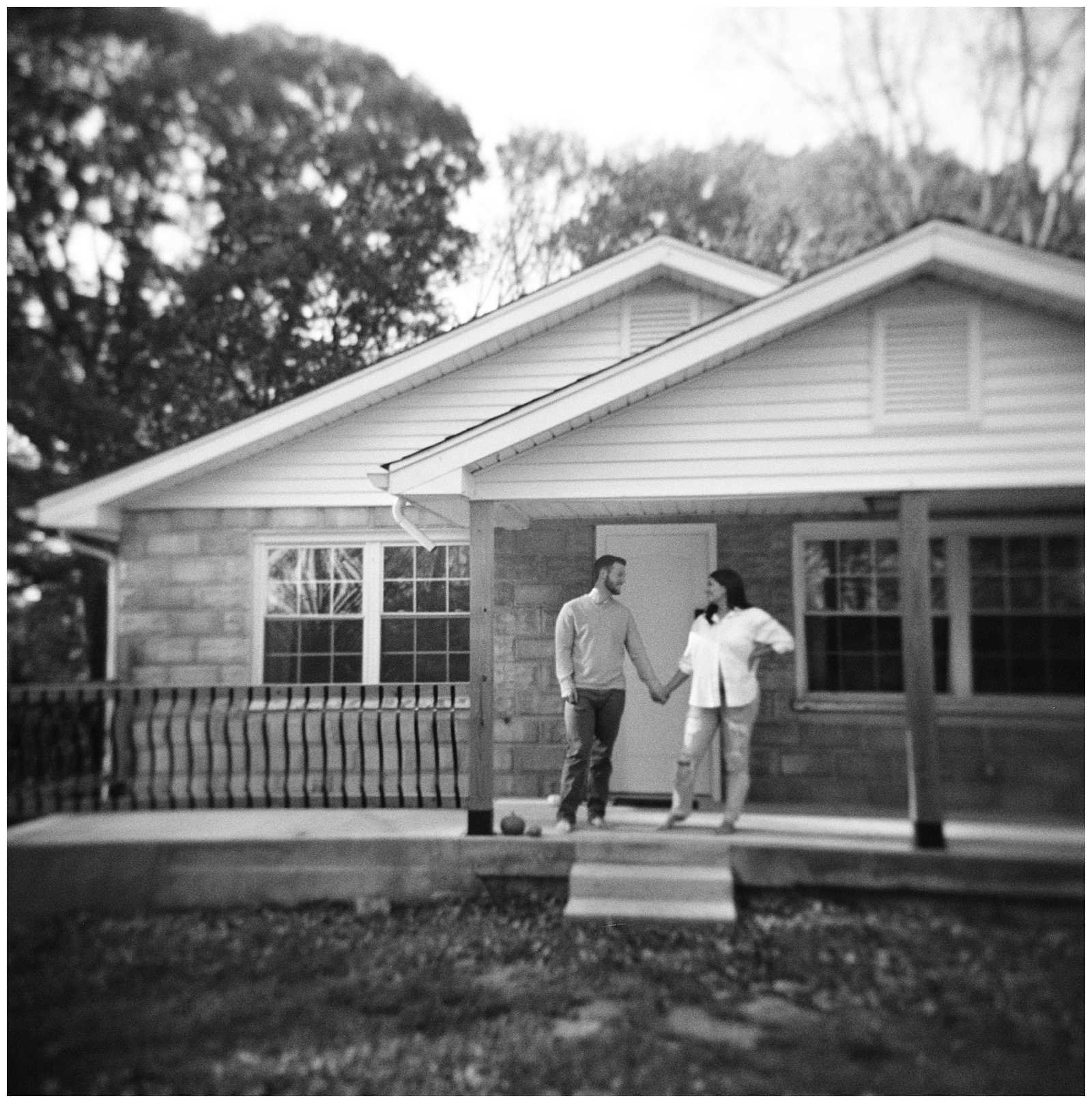 Black and white film image of mom and dad posing on the front porch of their first home during Knoxville maternity session.