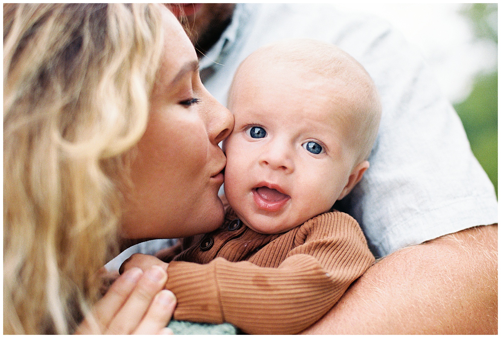 Mom kisses newborn on cheek at Lake Michigan during outdoorsy and gloomy family session