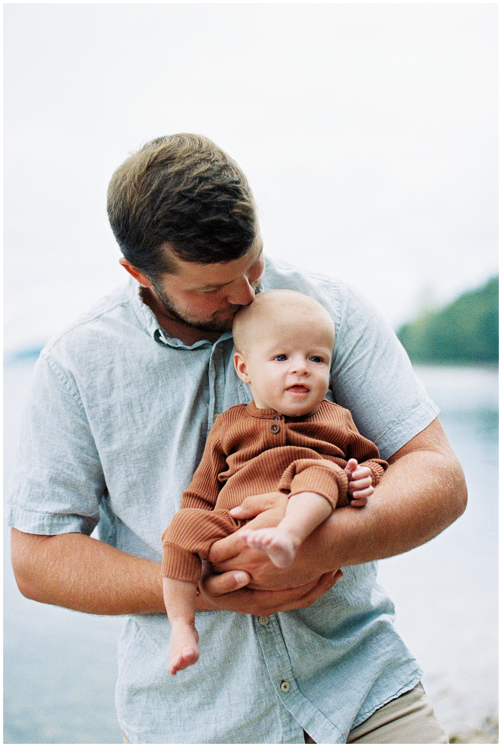 Dad kisses baby in front of Lake Michigan for relaxed family session