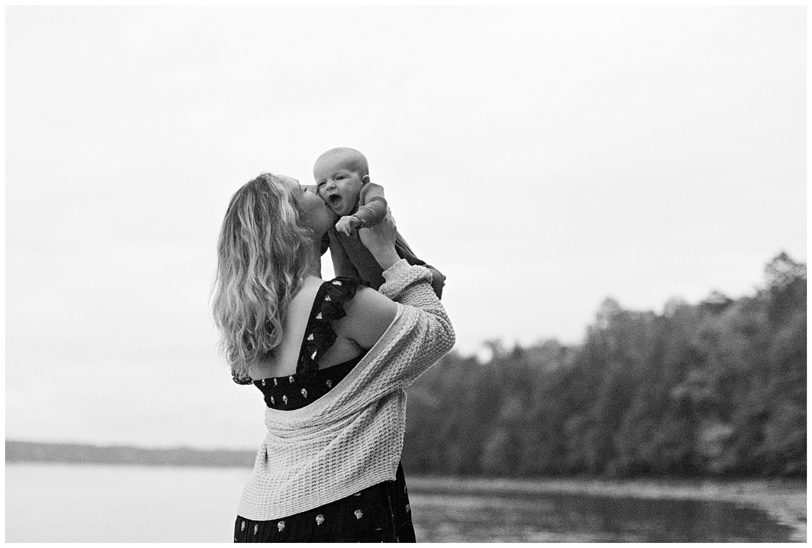 Black and white image of mom kissing baby on cheek in front of Lake Michigan