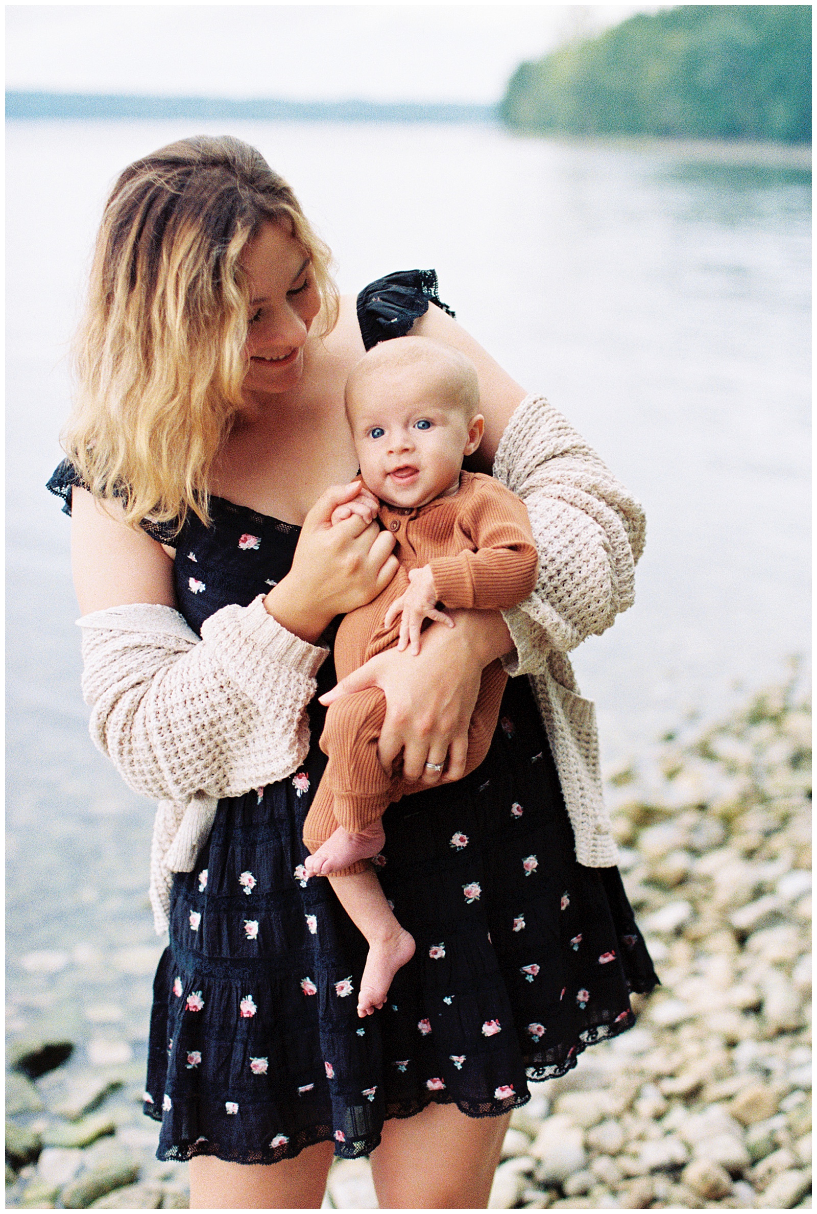 Mom and adorable newborn baby pose in front of lake for relaxed family session