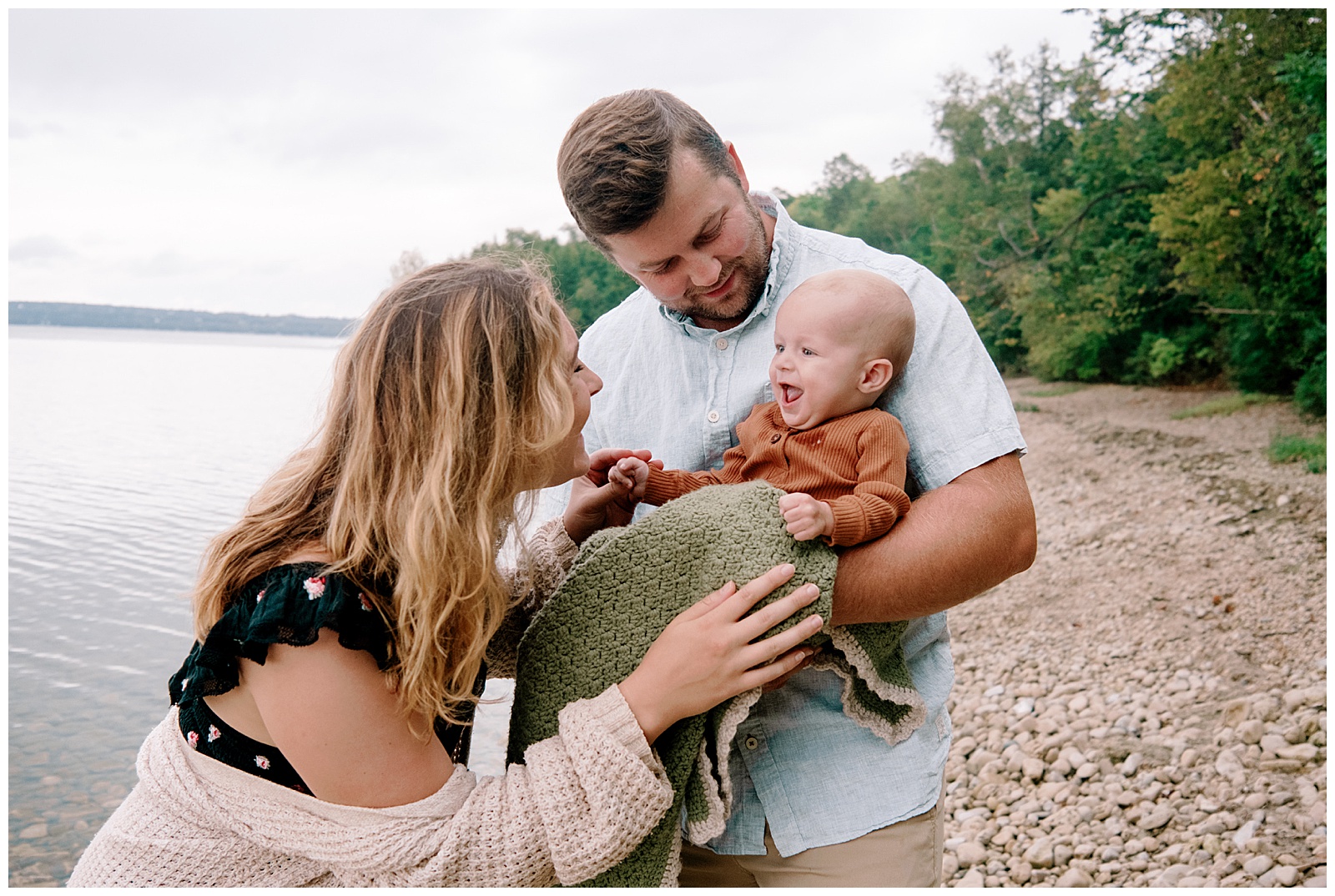 Mom and baby laugh together with Dad looking on for relaxed family session