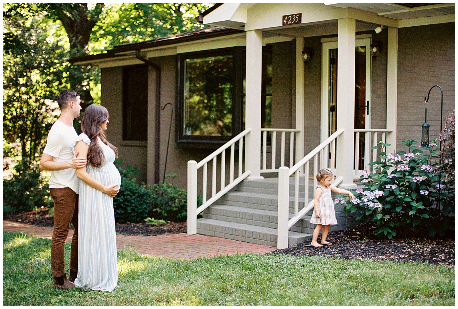 Dad and mom watch daughter pick flowers for an in-home knoxville maternity session