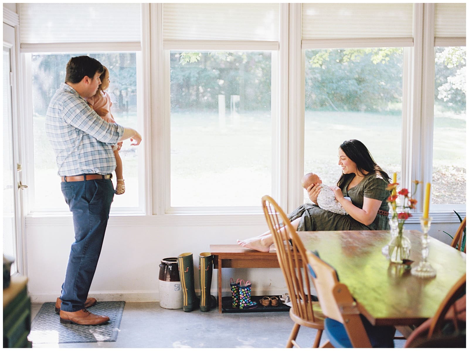 Mom and dad snuggle their newborn baby with big sister in their sunroom in home during their beautiful and light filled Knoxville area newborn session. 